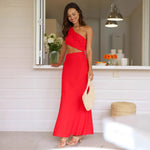 A woman wearing a sleeveless, solid red midi dress with an oblique collar. The dress has a long, flowing skirt, and she is standing in a resort-style setting.
