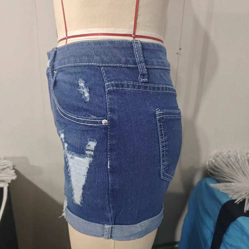A model wearing deep blue, high-waisted denim shorts with a cuffed hem, paired with a white t-shirt. The frayed edges of the shorts are visible, and the overall style is casual and chic.