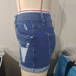 A model wearing deep blue, high-waisted denim shorts with a cuffed hem, paired with a white t-shirt. The frayed edges of the shorts are visible, and the overall style is casual and chic.