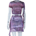 A woman wearing a purple fitted dress with a ruffle hem short top and matching mini skirt set, posing confidently.