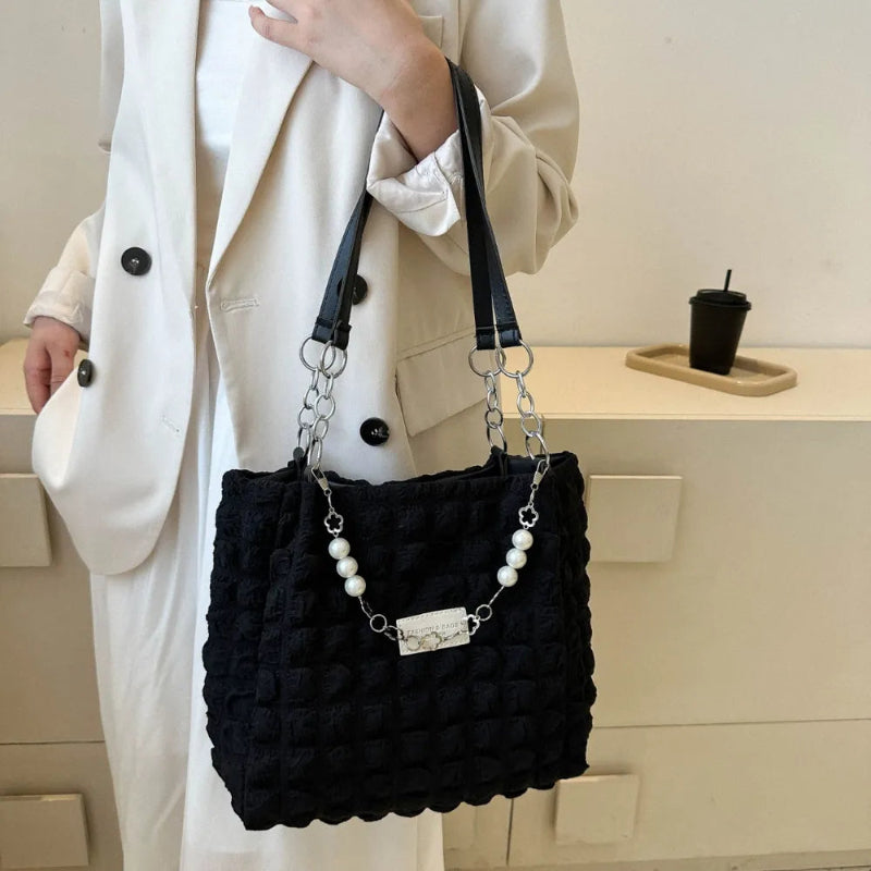 A close-up shot of a black bubble-textured tote bag with a chain detail, showcasing its unique surface and practical design.