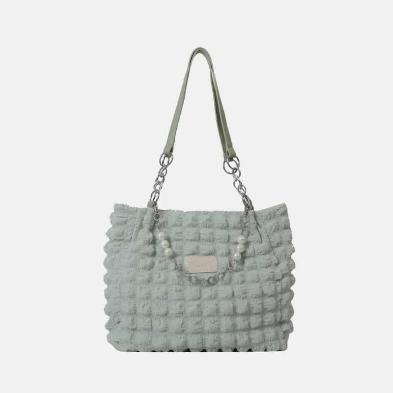 A close-up shot of a black bubble-textured tote bag with a chain detail, showcasing its unique surface and practical design.