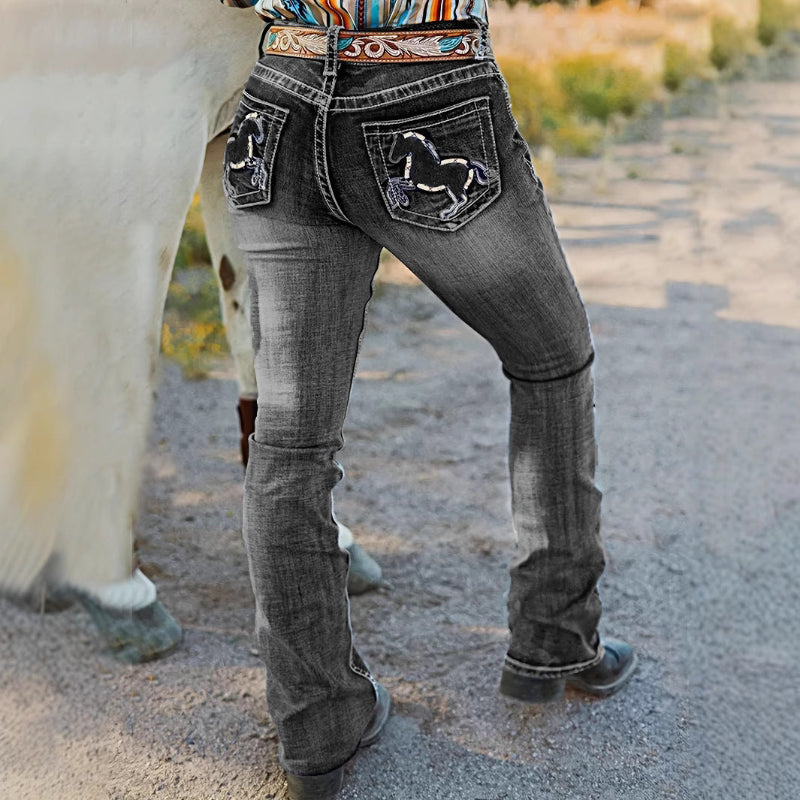 A pair of dark blue, high-waist, straight-leg denim jeans with subtle embroidery and a tie-dye gradient effect. The jeans are displayed flat, showcasing the style and texture.