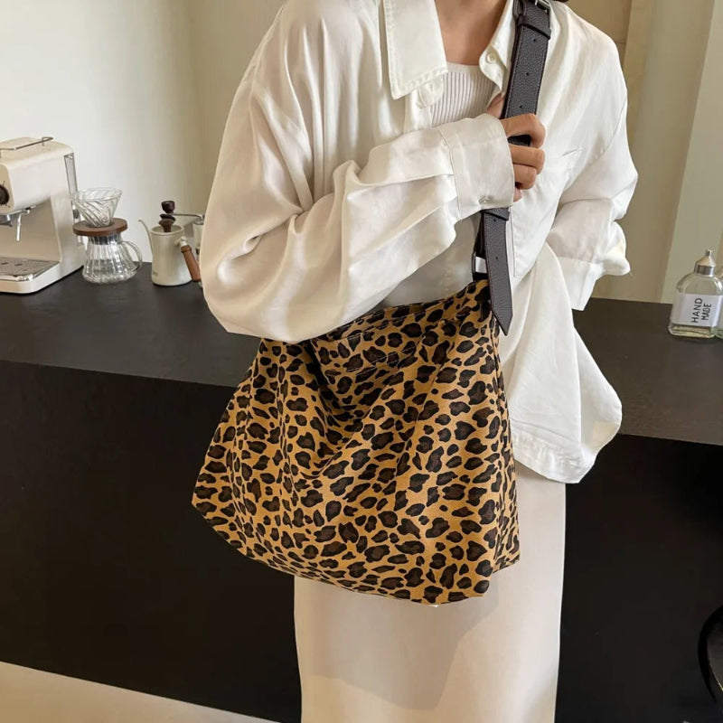 Close-up of a leopard print canvas tote bag with an adjustable strap, zipper closure, and visible interior pockets, displayed in a casual setting.