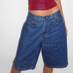 A pair of dark blue, mid-length, vintage-style denim shorts with a distressed finish. The shorts are laid flat, showcasing the straight-leg cut and medium-rise waist.