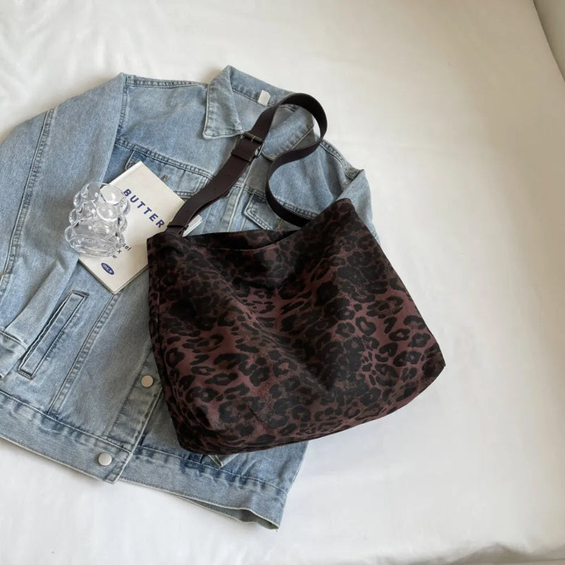 Close-up of a leopard print canvas tote bag with an adjustable strap, zipper closure, and visible interior pockets, displayed in a casual setting.