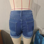 A model wearing deep blue, high-waisted denim shorts with a cuffed hem, paired with a white t-shirt. The frayed edges of the shorts are visible, and the overall style is casual and chic.