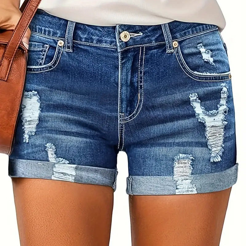 A model wearing deep blue, high-waisted denim shorts with a cuffed hem, paired with a white t-shirt. The frayed edges of the shorts are visible, and the overall style is casual and chic.
