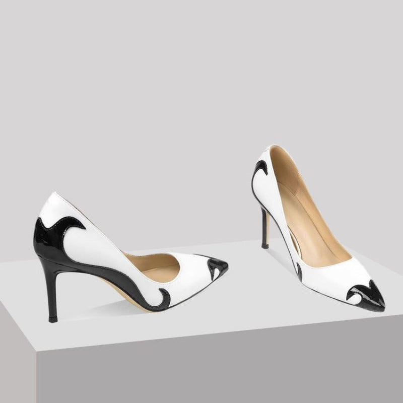 A close-up of a black satin high heel shoe with a pointed toe and a slender heel, featuring an embroidered white skull pattern and a dragonfly embellishment on the side.