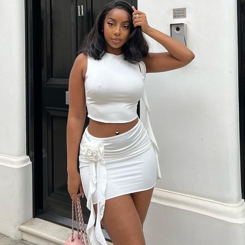  A woman wearing an embroidered flower round neck crop top and matching mini skirt set, smiling.