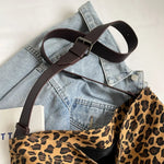 Close-up of a leopard print canvas tote bag with an adjustable strap, zipper closure, and visible interior pockets, displayed in a casual setting.
