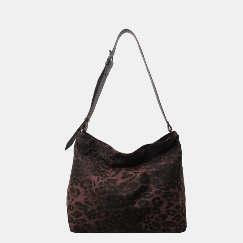 Close-up of a leopard print canvas tote bag with an adjustable strap, zipper closure, and visible interior pockets, displayed in a casual setting.