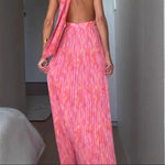 A woman from behind wearing a pink, backless, sleeveless midi dress with V-lace detailing on the back.