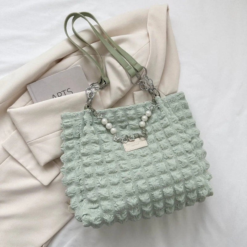 A close-up shot of a black bubble-textured tote bag with a chain detail, showcasing its unique surface and practical design.