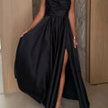 A black pleated strapless A-line midi dress with a side slit, displayed on a mannequin, highlighting its elegant design and flow.