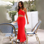 A woman wearing a sleeveless, solid red midi dress with an oblique collar. The dress has a long, flowing skirt, and she is standing in a resort-style setting.