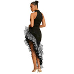 A full-length image of a woman wearing a black, sleeveless, mid-length dress with sequined lace detailing, a round neck, and an irregular hem.