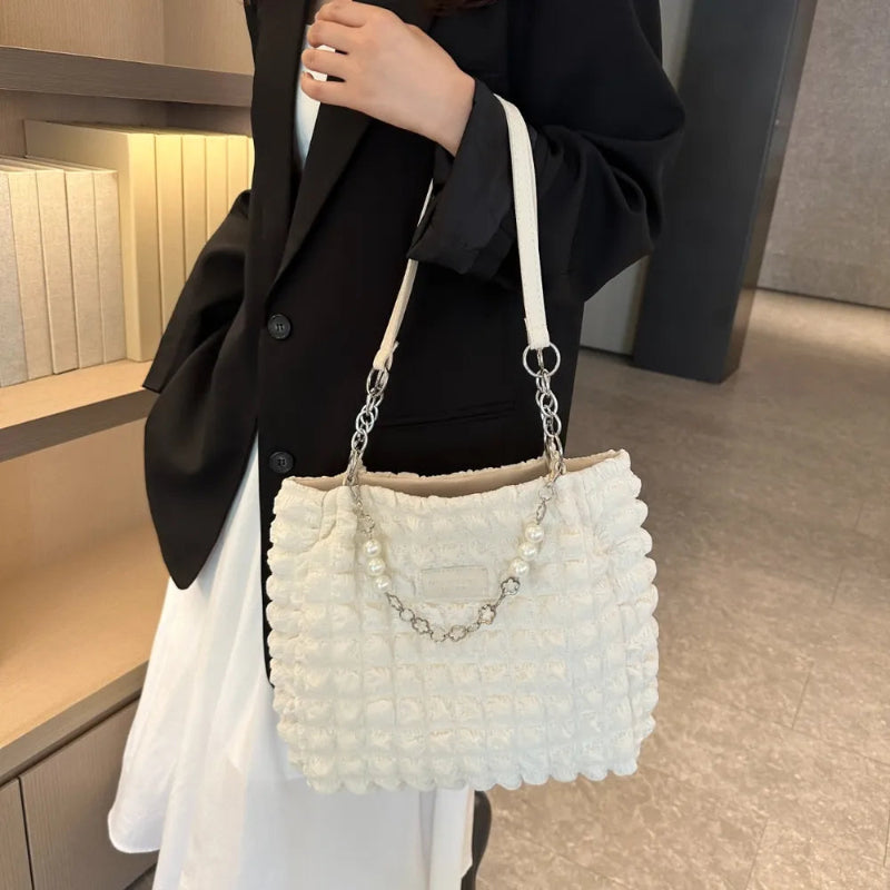 A close-up shot of a black bubble-textured tote bag with a chain detail, showcasing its unique surface and practical design.