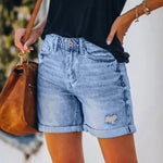A pair of blue, high-waisted fringed denim shorts with distressed details. The shorts are laid flat on a neutral background, showcasing the style and texture. The fringe detailing is prominent along the hemline.