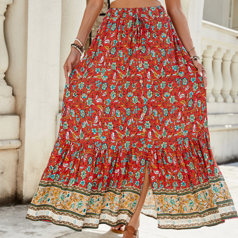 A high-waisted midi skirt with a bold digital print and a daring side slit, shown in a dark blue color. The skirt has snap buttons and is styled with a simple top.