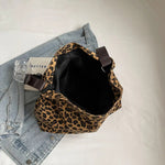Close-up of a leopard print canvas tote bag with an adjustable strap, zipper closure, and visible interior pockets, displayed in a casual setting.