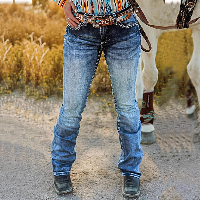 A pair of dark blue, high-waist, straight-leg denim jeans with subtle embroidery and a tie-dye gradient effect. The jeans are displayed flat, showcasing the style and texture.