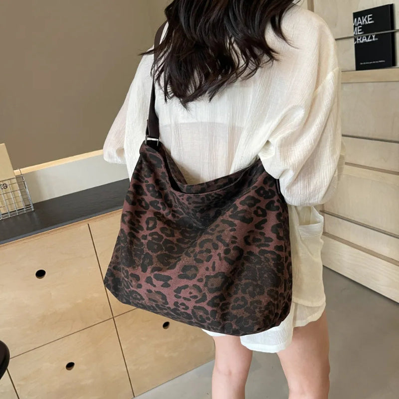 Close-up of a leopard print canvas tote bag with an adjustable strap, zipper closure, and visible interior pockets, displayed in a casual setting.