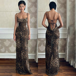 A woman confidently posing in a long, sleeveless maxi dress with a bold leopard print. The dress features a dramatic backless design and flows elegantly to the ground.