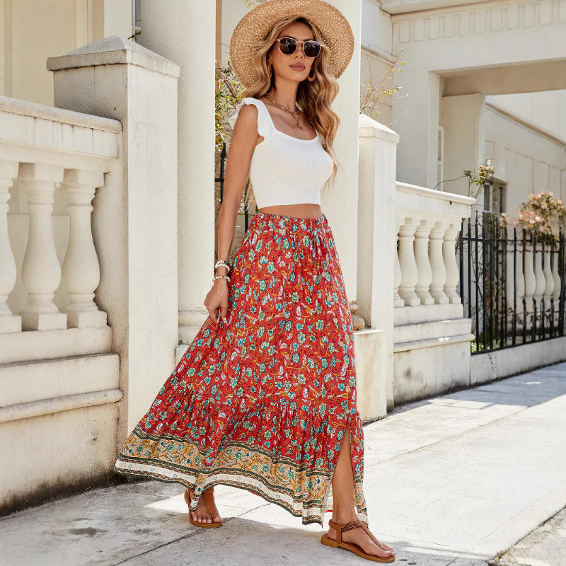 A high-waisted midi skirt with a bold digital print and a daring side slit, shown in a dark blue color. The skirt has snap buttons and is styled with a simple top.