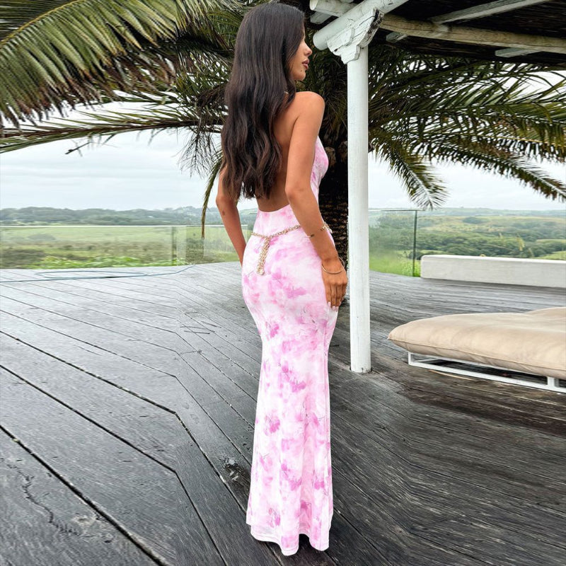 A woman wearing an elegant, form-fitting maxi dress with a sheer mesh fabric and a vibrant print. The dress has a halter neckline and a gathered waist.
