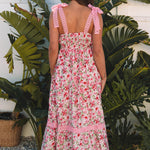 Woman wearing a floral dress with pink ruffled straps standing in front of green plants.