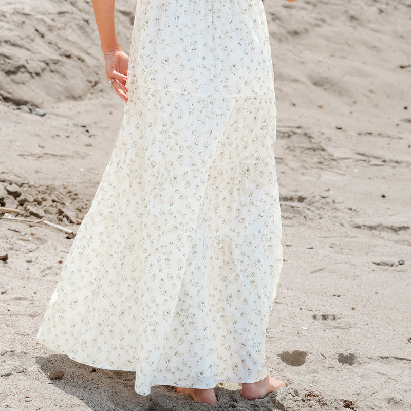 Woman in a white dress standing on a sandy beach.