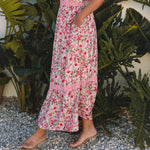 Woman in a pink floral dress standing in front of tropical plants
